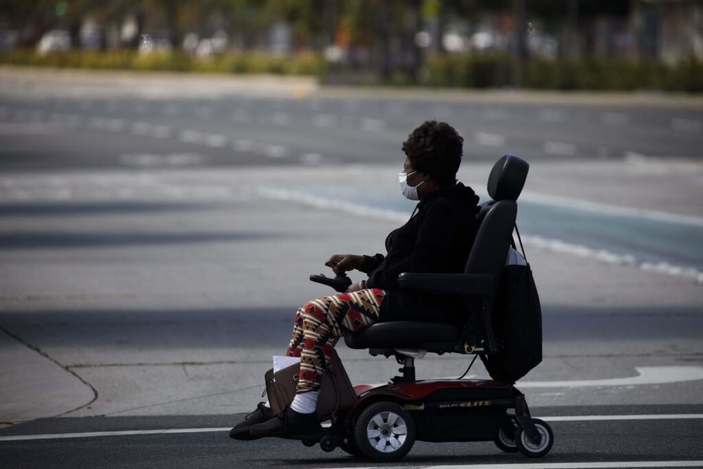 Woman in a motorized wheelchair crossing a wide street at a crosswalk