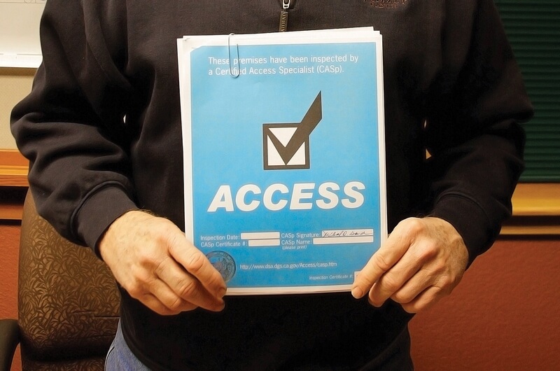 Man holding a blue CASp notice reading 'These premises have been inspected by a Certified Access Specialist'