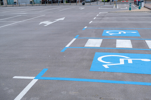 Accessible parking spaces marked with blue paint, wheelchair symbols, and a striped crosswalk in an outdoor lot