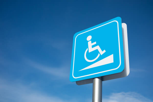 Blue accessible parking sign with the International Symbol of Accessibility mounted on a metal post against a clear sky